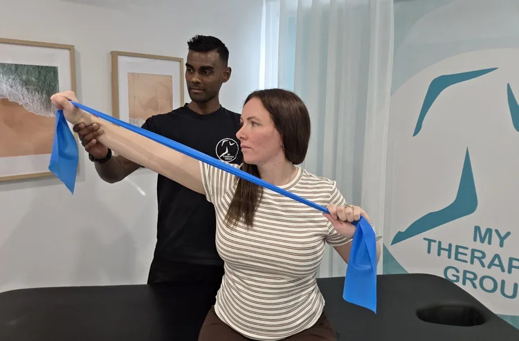 Ash guiding a resistance-band shoulder exercise.